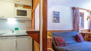 A compact kitchen with a microwave, sink, and a small refrigerator. There is a wooden bench with cushions and a framed picture on the wall. - **Cozy Ski-In/Ski-Out Apartment Near Children's Village, Sleeps 5** (Val-d'Isère)