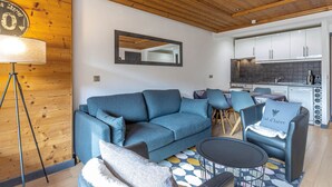 A modern living room with a blue sofa, a small round table, and a coffee table. There is a wooden ceiling and a kitchen in the background. - Elegant apartment in Val-d'Isère with balcony, parking, wifi (Val-d'Isère)