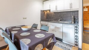 A compact kitchen with white cabinets, a built-in oven, and a sink. There is a dining table with a patterned tablecloth and chairs. - Elegant apartment in Val-d'Isère with balcony, parking, wifi (Val-d'Isère)