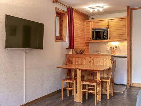 A compact kitchen with wooden cabinets, a microwave, a sink, and a dining area with a table and chairs. - Charming Studio with Parking, Ski-In/Ski-Out in Central Val-d'Isère (Val-d'Isère)