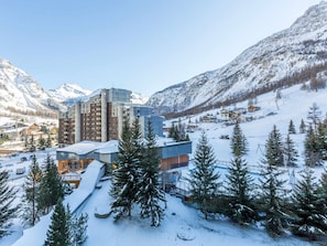 A modern hotel with a ski slope view, surrounded by snow-covered mountains and pine trees.