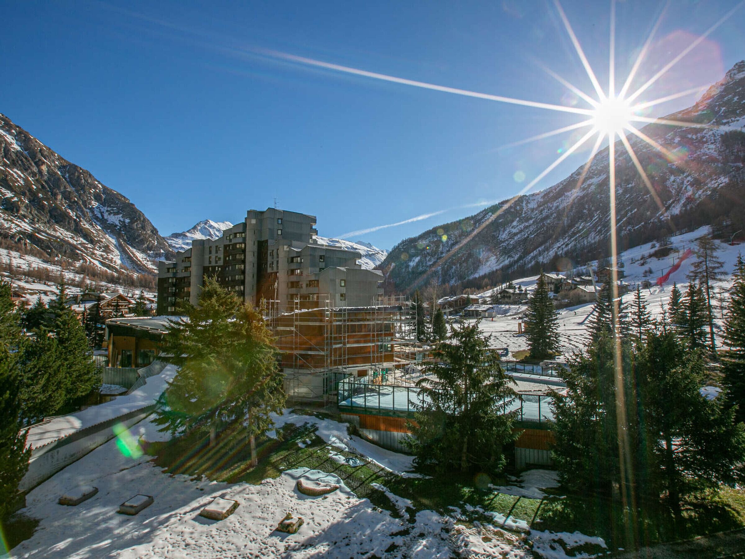 A modern hotel with multiple floors, surrounded by snow-covered mountains and pine trees.