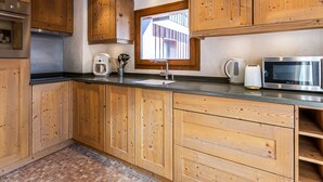 Een keuken met houten kastjes, een roestvrijstalen koelkast, een koffiezetapparaat, een magnetron en een raam met uitzicht.