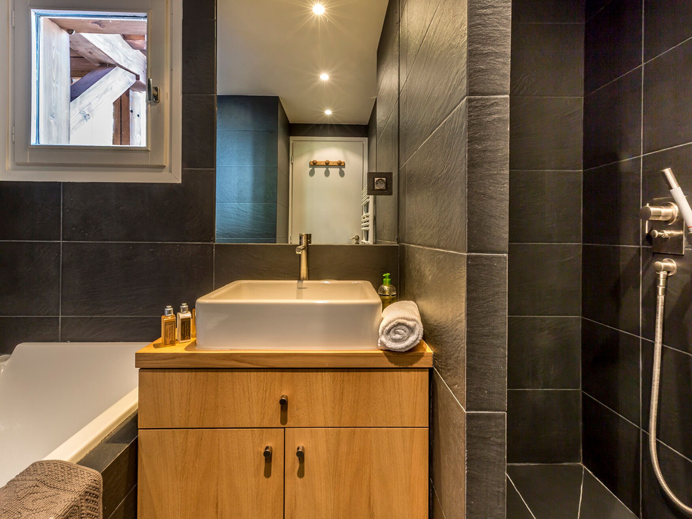 Un baño moderno con tocador de madera, un lavabo blanco y zona de ducha.