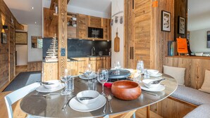 A dining area with a round table set for four, surrounded by wooden walls and a kitchen in the background. - Luxury Chalet Apartment, Ski-In/Ski-Out, Val-d’Isère (Val-d'Isère)