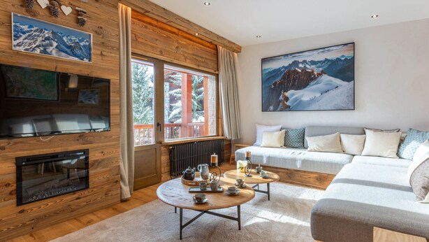 A cozy living room with a fireplace, a sofa, a coffee table, and a large window with a view of snow-covered mountains. - Luxury Chalet Apartment, Ski-In/Ski-Out, Val-d’Isère (Val-d'Isère)