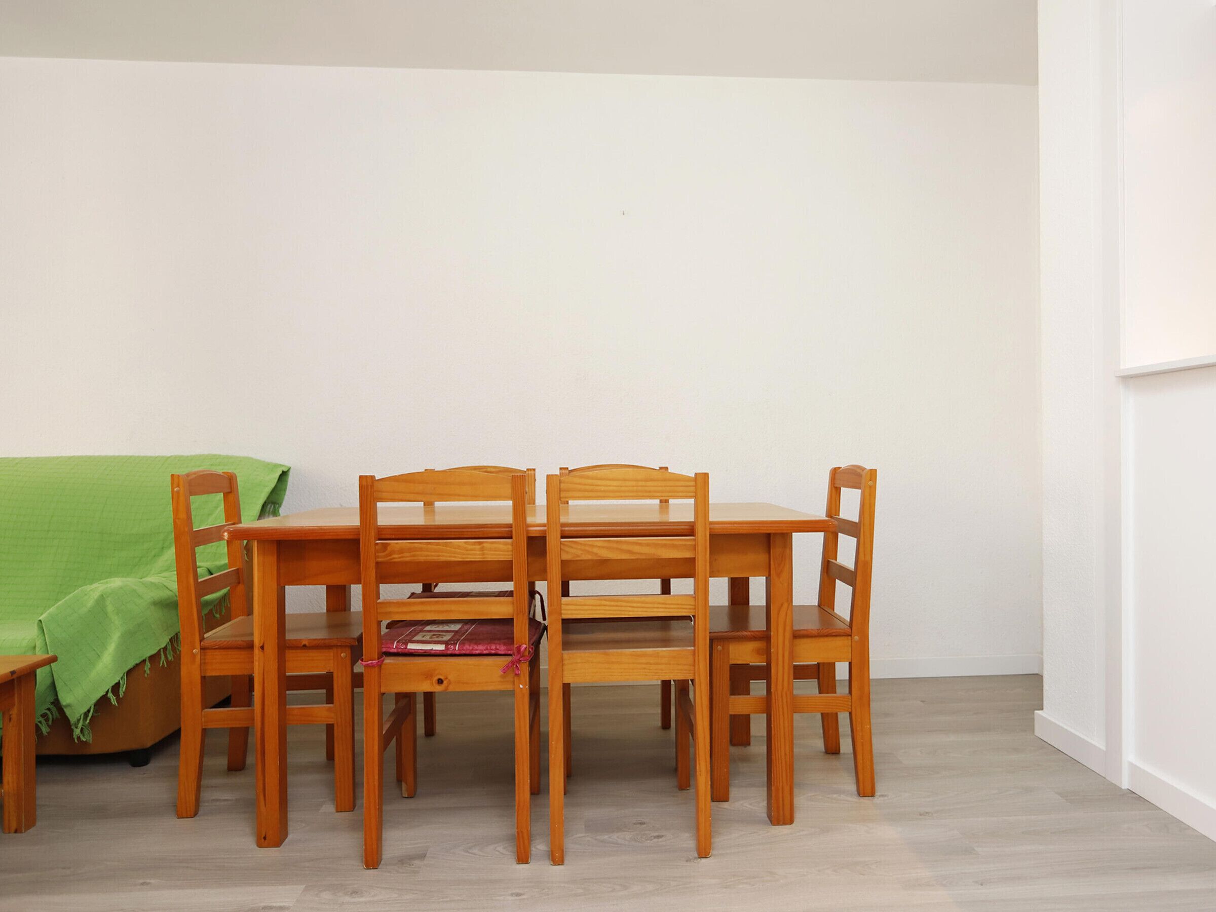 Un comedor con una mesa de madera y cuatro sillas, un cubre sofá verde y una pared blanca.