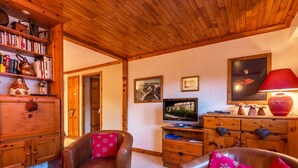 Uma sala de estar acolhedora com poltronas de couro, estante de madeira, televisão e abajur vermelho.