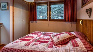 Quarto com uma cama grande, teto de madeira e janela com cortinas.