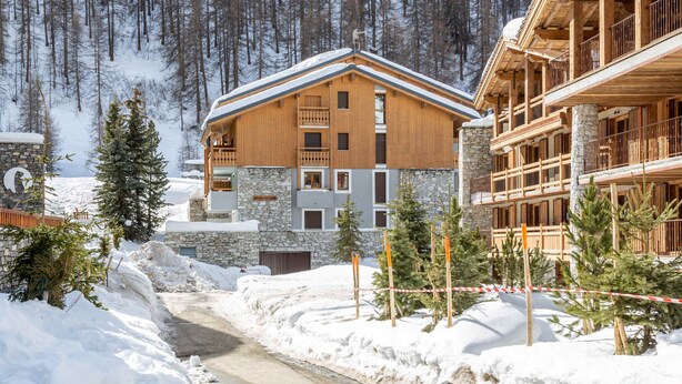 En trælodge med stenvægge, en snedækket sti og et skilt med teksten "LE VAL BLANC".
