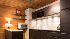 A modern kitchen with dark cabinets, a microwave, and a sink. There is a wooden ceiling and a shelf with decorative items. - Luxury apartment in the center, pets allowed, WiFi (Val-d'Isère)