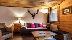 A cozy room with a wooden ceiling, a sofa with colorful cushions, a wooden table, and a wall-mounted deer head decoration. - Luxury apartment in the center, pets allowed, WiFi (Val-d'Isère)