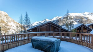 Una cabaña de madera con un porche cubierto de nieve y montañas al fondo.