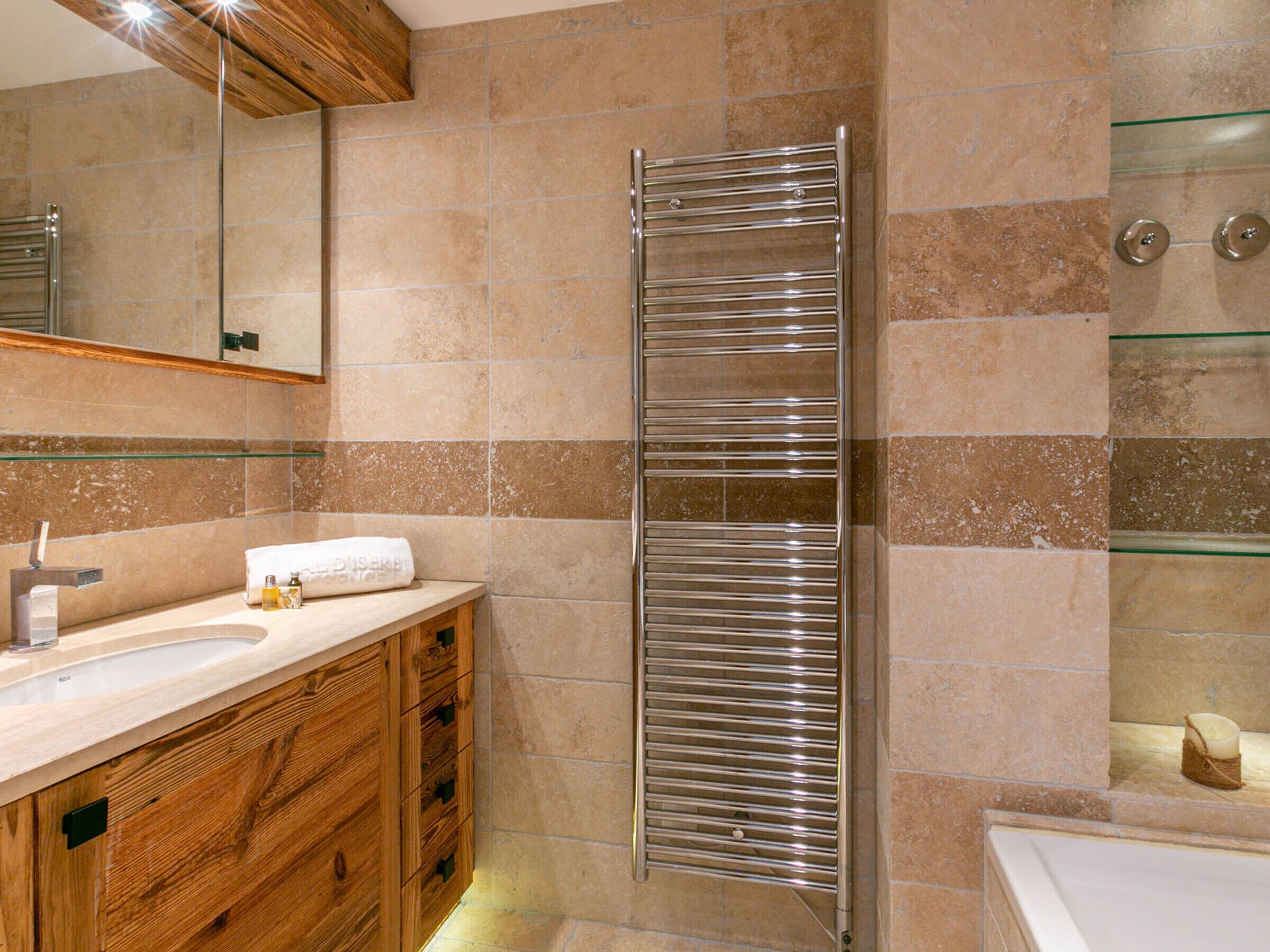 Un bagno moderno con un mobile vanitario in legno, cabina doccia in vetro e porta asciugamani integrata.