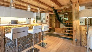 Une cuisine moderne avec un mur de crédence en pierre, des tabourets de bar blancs et un escalier en bois.