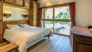 Une chambre à coucher en bois, avec un grand lit, une table de chevet, un bureau et une fenêtre donnant sur un paysage montagneux.