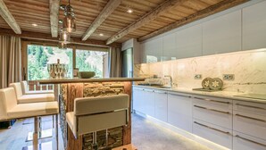 Une cuisine moderne avec un mur d’accent en pierre, un plafond en bois et une grande fenêtre offrant une vue sur l’extérieur.