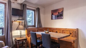 Una stanza accogliente con una panca e un tavolo di legno, una TV fissata al muro e una finestra con tende.