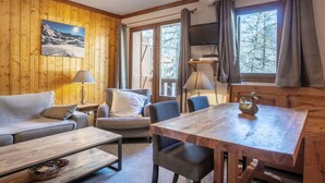 Un accogliente interno di una baita con arredamento in legno, un divano, un tavolo da pranzo e un televisore.