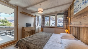 Een slaapkamer met een bed, een televisie, een raam met gordijnen en uitzicht op de omgeving.