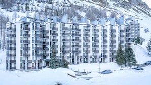 Een modern meerlaags hotel met balkons, gelegen voor een besneeid berglandschap.