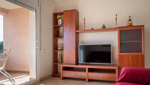 Una sala de estar moderna con televisor de pantalla plana, estanterías de madera, una mesa de centro de vidrio y un sofá rojo.