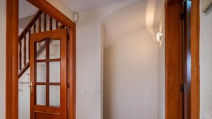 Un pasillo con una puerta de madera, una escalera y un interruptor de luz en la pared.