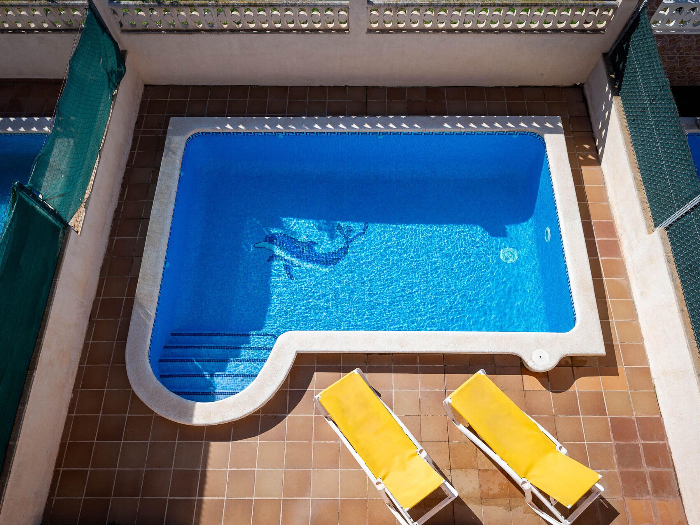 A rectangular swimming pool with a blue interior, surrounded by a white border. There are two yellow lounge chairs placed on the poolside.