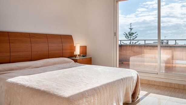 Habitación de hotel con una cama grande, una mesita de noche con lámpara y vistas al cielo y a un árbol a través de una puerta corrediza de vidrio.