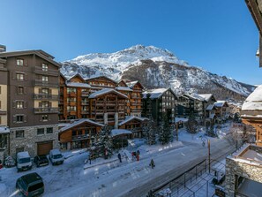 A snow-covered mountain resort with multi-story buildings, including wooden cabins and a hotel with balconies.