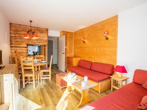 Ein gemütliches Zimmer mit einer Holzwand, einem Sofa, einem Esstisch mit Stühlen und einem Fernseher.