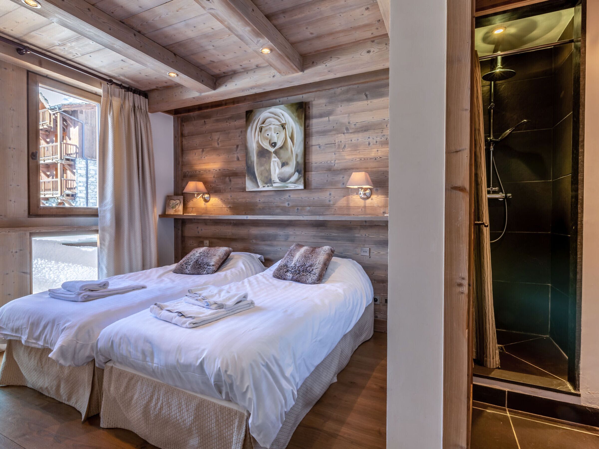 A room with two beds, wooden walls, a painting, and a shower area.