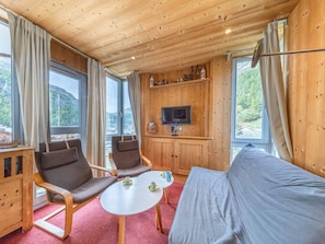 A cozy cabin interior with wooden walls, a sofa, two armchairs, a small table, and a television.
