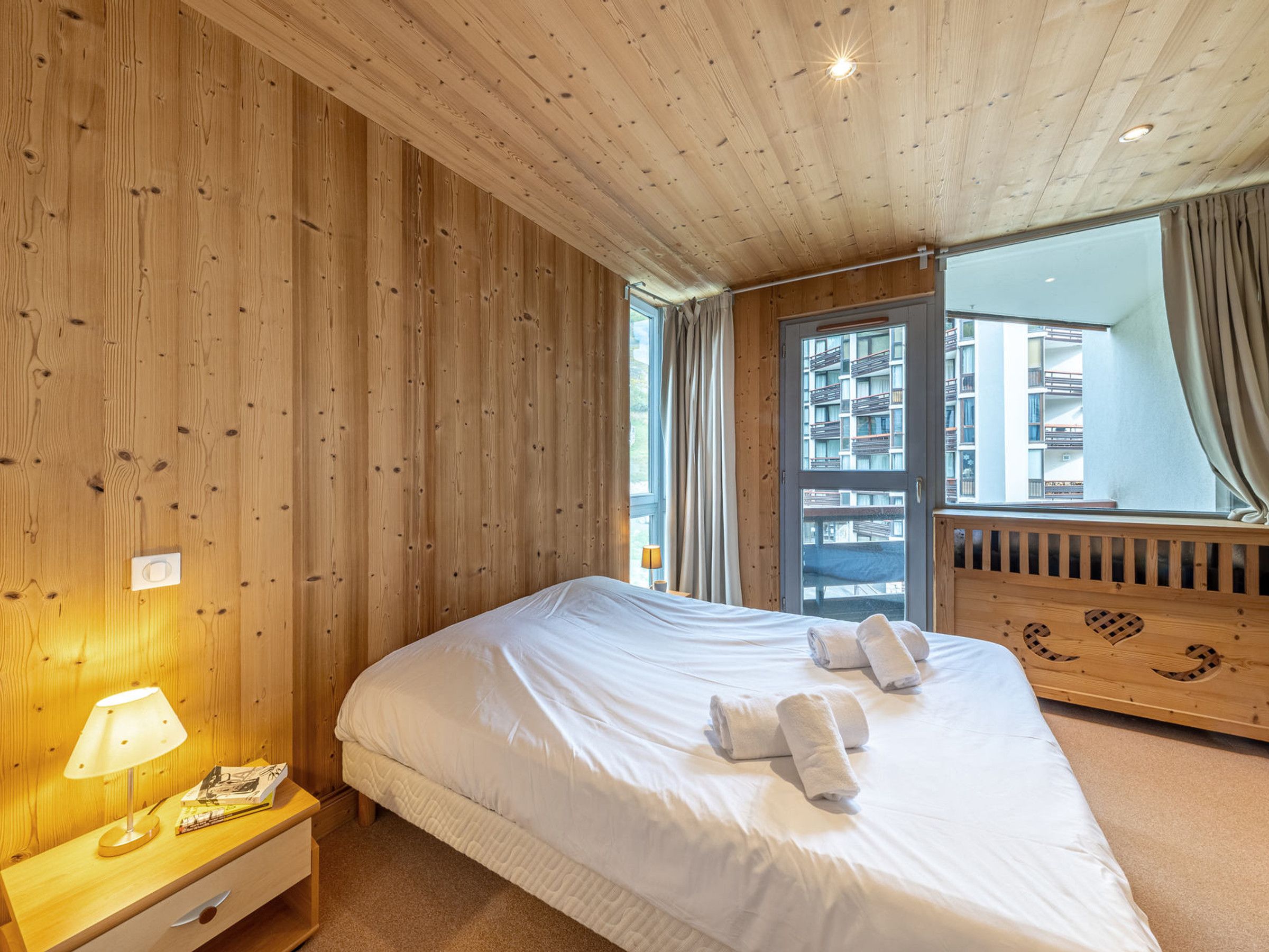 Habitació d'hotel amb sostre de fusta, un llit gran amb llençols blancs, una tauleta de nit amb una làmpada i una finestra amb cortines.