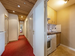 A narrow hallway with a red carpet leading to a kitchen area with wooden cabinets and a white stove.