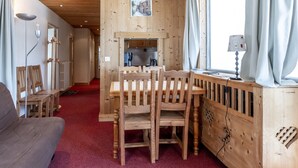 Un interior de madera con un comedor, un sofá y una cocina visible a través de un umbral abierto.