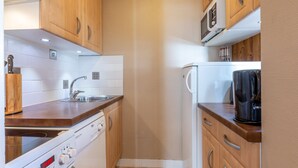 Una kitchenette compacta con armarios de madera, microondas integrado, cafetera y lavavajillas.