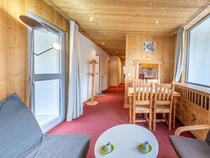 A cozy room with a wooden ceiling, a dining table with chairs, a sofa, and a window with curtains.