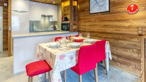 A dining area with a wooden interior, a kitchen with modern appliances, and a framed map on the wall. - Spacious 3-BR Duplex with South Balcony, WiFi, Parking, Ski Storage, Near Slopes (Val-d'Isère)