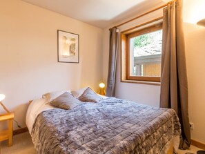 Quarto com cama, mesa de cabeceira, abajur, janela com cortinas e um quadro na parede.