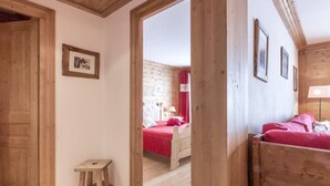 A wooden room with a bed, a small stool, and a framed picture on the wall.