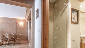 A wooden interior with a glass-enclosed shower, a dining area with wooden chairs, and a framed picture on the wall.