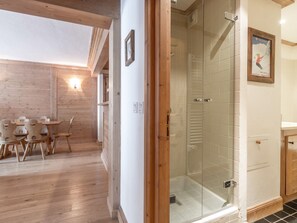 A wooden interior with a glass-enclosed shower, a dining area with wooden chairs, and a framed picture on the wall.