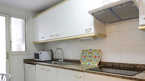 A kitchen with white cabinets, a microwave, a sink, and a patterned cutting board. - Beachfront apartment with pool and parking, Torredembarra (Torredembarra)