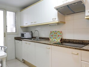 A kitchen with white cabinets, a microwave, a sink, and a patterned cutting board.
