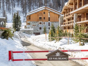 Een houten lodge met stenen muren, een sneeuw bedekte pad en een bordje met de tekst 'LE VAL BLANC'.