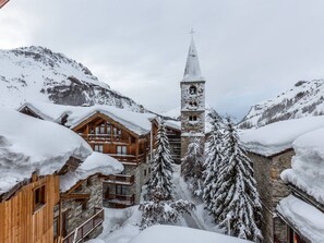 Un villaggio montano innevato con edifici in legno e una torre campanaria.