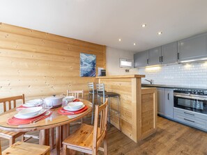 A modern kitchen with wooden cabinetry, a central island, and a dining area with a glass table and wooden chairs.
