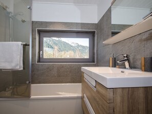 A modern bathroom with a bathtub, a large mirror, and a window with a mountain view.