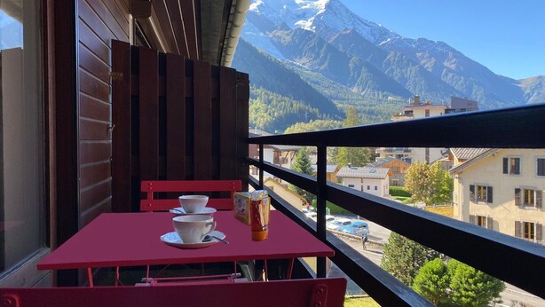 Ein Balkon mit rotem Tisch und Stühlen, einem Fenster und Blick auf einen Berg.